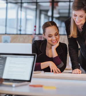 Two young woman at office working on a new creative design. Diverse team of professionals looking at a document smiling.